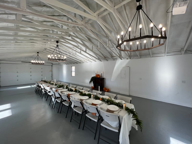 Indoor event hall at Rio Viejo Events with a long candlelit dinner table, black iron chandeliers and a ceiling projector